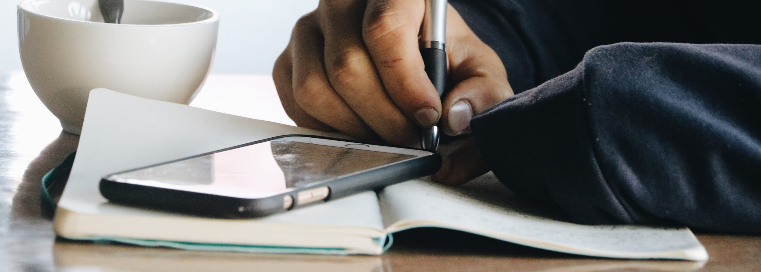 Person writing with a mobile phone on a table